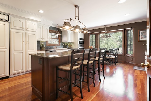 kitchen featuring a center island, backsplash, wood finished floors, a breakfast bar area, and double oven