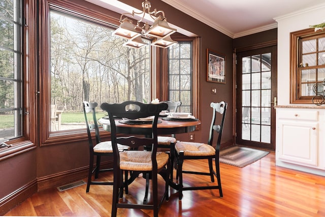 dining area featuring light wood-type flooring, baseboards, visible vents, a notable chandelier, and crown molding