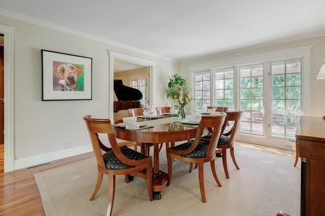dining room with light wood-type flooring, baseboards, visible vents, and crown molding