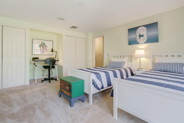 bedroom featuring two closets, visible vents, and light colored carpet