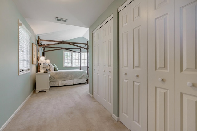 bedroom featuring vaulted ceiling, multiple closets, light carpet, baseboards, and visible vents