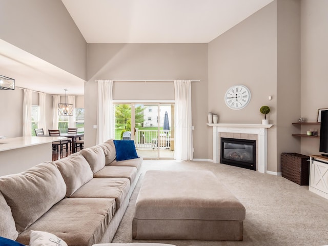 carpeted living room featuring a chandelier, a tile fireplace, a towering ceiling, and baseboards