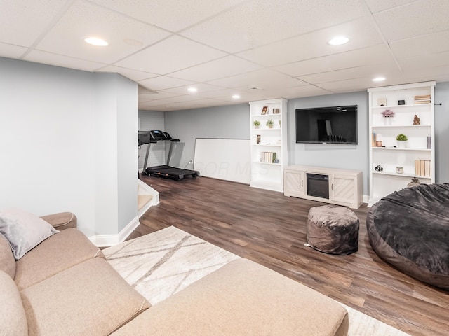 living room with built in features, a glass covered fireplace, recessed lighting, wood finished floors, and baseboards