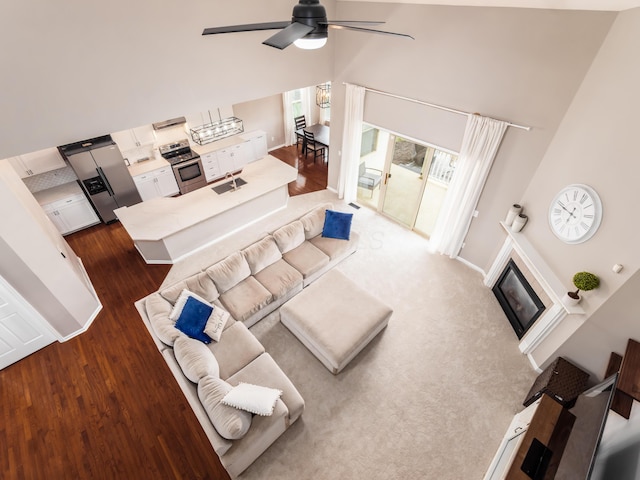 living room with dark wood finished floors, ceiling fan, a towering ceiling, and a glass covered fireplace