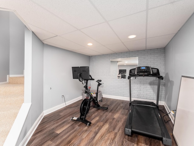 exercise room featuring baseboards, brick wall, recessed lighting, a drop ceiling, and wood finished floors