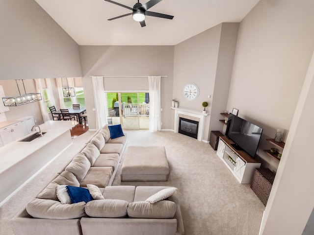 living room featuring high vaulted ceiling, a fireplace, a ceiling fan, light carpet, and baseboards