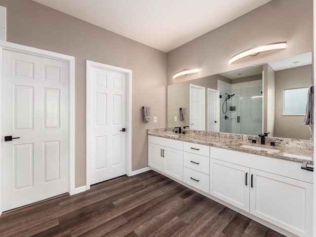 bathroom featuring a stall shower, wood finished floors, double vanity, and a sink