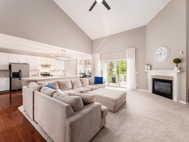 living area featuring baseboards, a ceiling fan, dark wood-type flooring, high vaulted ceiling, and a tile fireplace