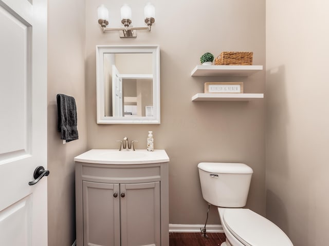 bathroom with toilet, wood finished floors, vanity, and baseboards