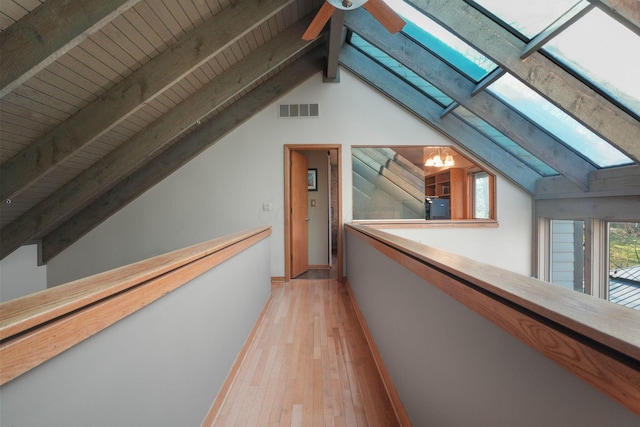 hallway featuring baseboards, visible vents, light wood-style flooring, and vaulted ceiling with skylight
