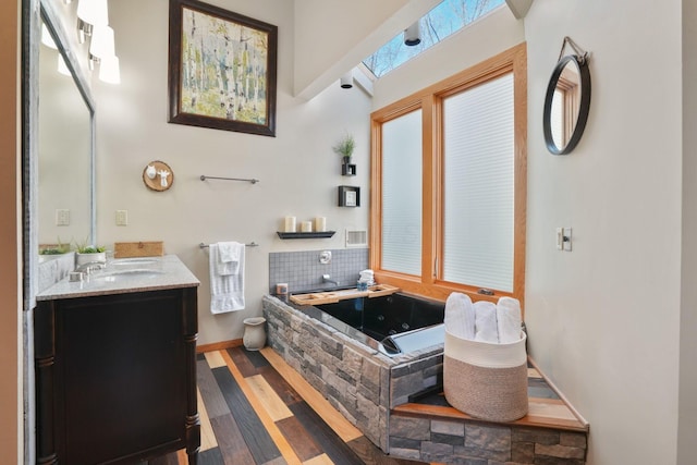 full bath with vanity, a garden tub, baseboards, and wood finished floors