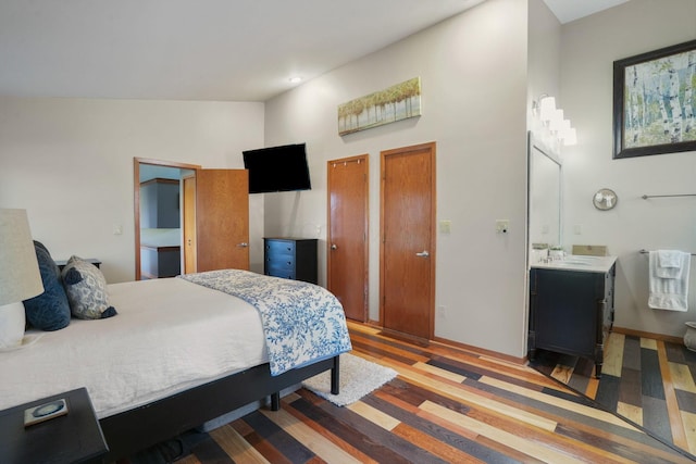bedroom with a high ceiling, ensuite bathroom, two closets, and wood finished floors