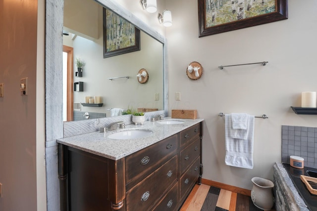 bathroom featuring a sink, baseboards, double vanity, and wood finished floors
