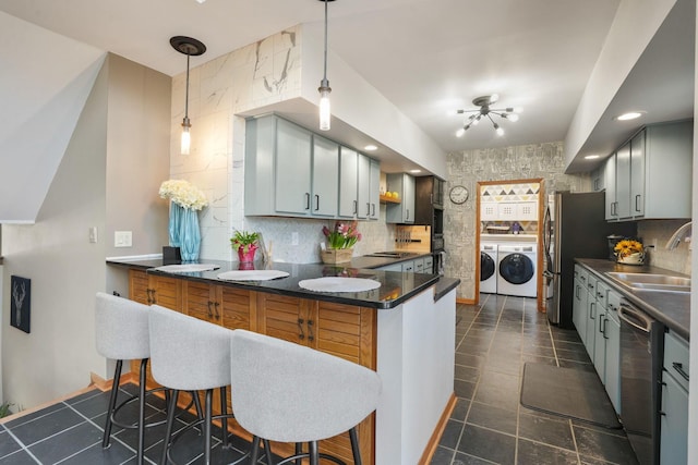 kitchen with independent washer and dryer, dark countertops, appliances with stainless steel finishes, a sink, and a peninsula