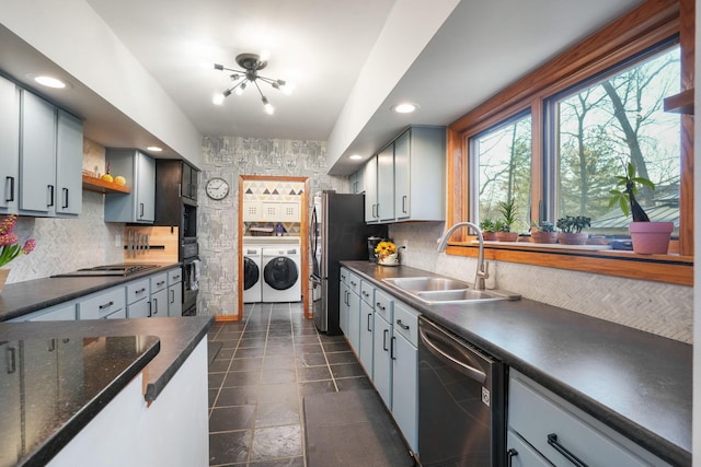 kitchen featuring decorative backsplash, dark countertops, separate washer and dryer, a sink, and appliances with stainless steel finishes