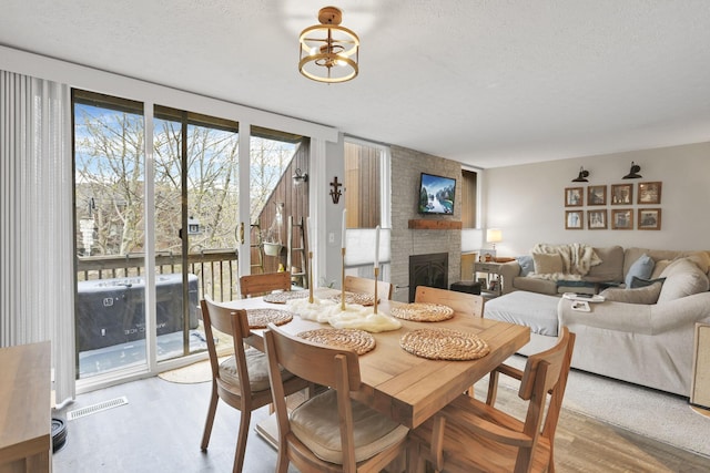 dining space with a textured ceiling, a fireplace, wood finished floors, and visible vents