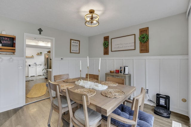dining area with a decorative wall, washer / clothes dryer, a wainscoted wall, and light wood-type flooring