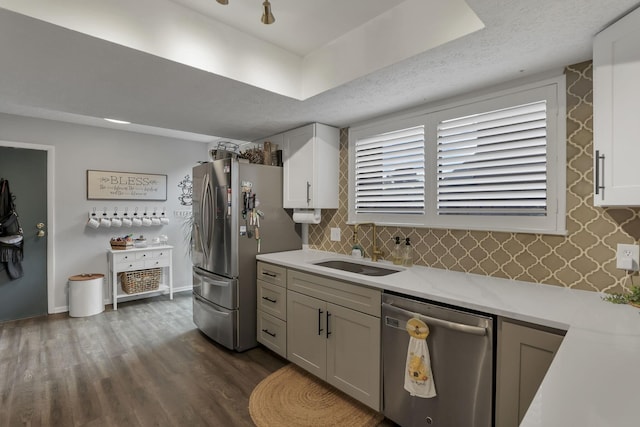 kitchen with light stone counters, appliances with stainless steel finishes, a sink, tasteful backsplash, and dark wood-type flooring
