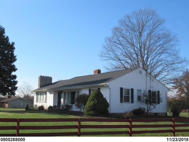 ranch-style home featuring a front lawn, a chimney, and fence