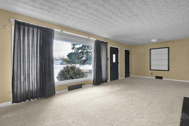 carpeted spare room featuring visible vents, baseboards, and a textured ceiling