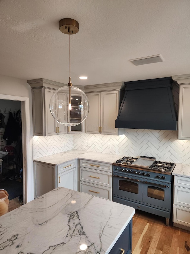 kitchen featuring range with two ovens, light stone counters, premium range hood, and tasteful backsplash