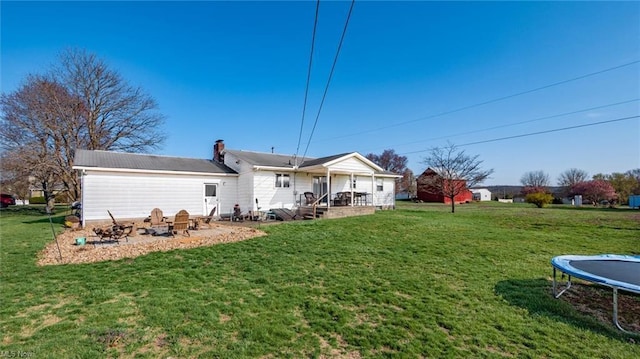 rear view of property featuring a chimney, an outdoor fire pit, a trampoline, a yard, and a patio area