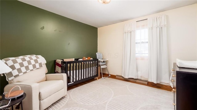 bedroom featuring wood finished floors, a nursery area, and a baseboard radiator