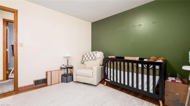 bedroom with wood finished floors, baseboards, a nursery area, and visible vents