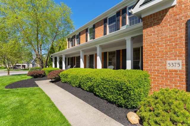 view of side of home with a lawn, a porch, and brick siding