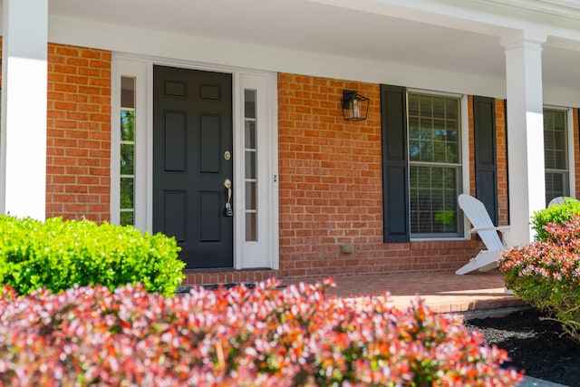 entrance to property featuring a porch and brick siding