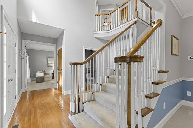 staircase featuring a high ceiling, baseboards, and wood finished floors