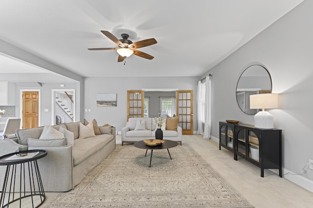 living area featuring a ceiling fan, stairway, light colored carpet, and baseboards