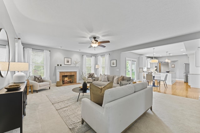 living area with light colored carpet, plenty of natural light, a warm lit fireplace, and ceiling fan