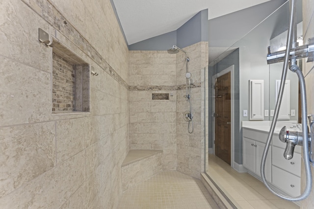 full bath featuring vaulted ceiling, vanity, tiled shower, and tile patterned floors