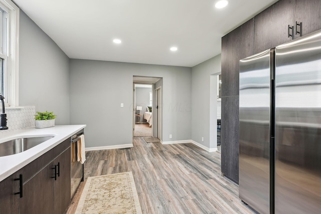 kitchen featuring light countertops, stainless steel appliances, dark brown cabinetry, a sink, and light wood-style floors