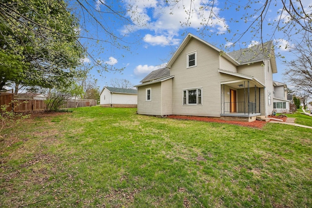 rear view of property featuring roof with shingles, fence, and a yard