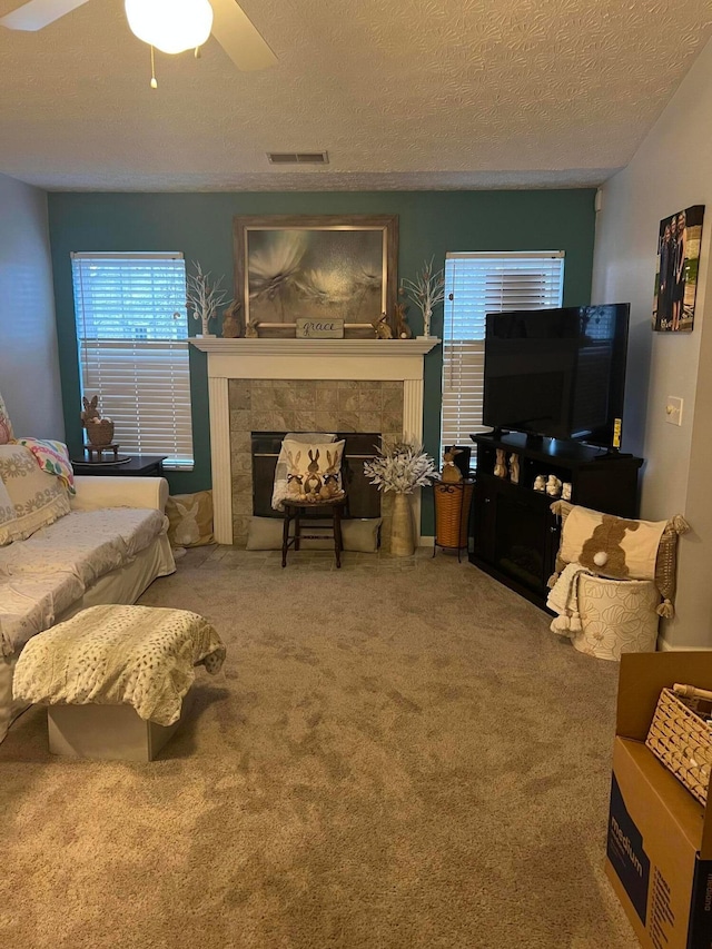 living room with carpet flooring, a fireplace, a textured ceiling, visible vents, and ceiling fan