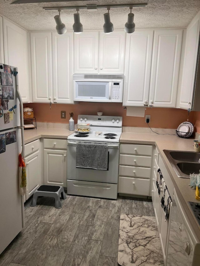 kitchen featuring white appliances, white cabinets, light countertops, and a sink
