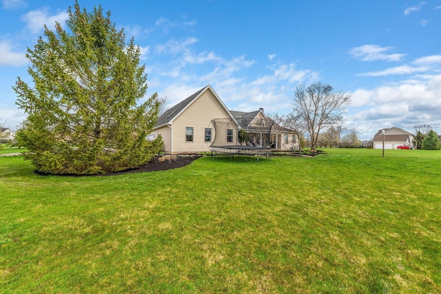 rear view of property featuring a trampoline and a lawn