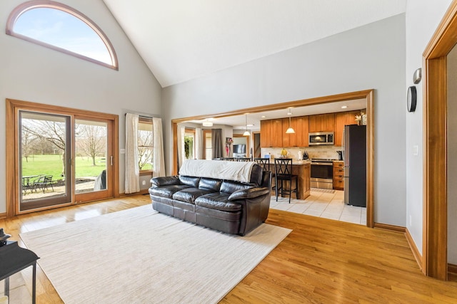 living area with light wood-style flooring, high vaulted ceiling, and baseboards
