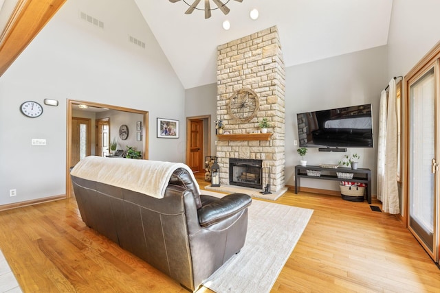living area featuring light wood-type flooring, visible vents, and a stone fireplace