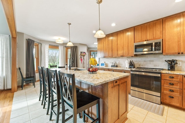 kitchen featuring light tile patterned floors, a sink, stainless steel appliances, a center island with sink, and decorative backsplash