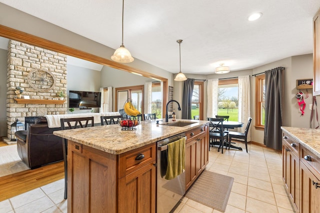 kitchen featuring light tile patterned floors, dishwasher, a sink, brown cabinetry, and a center island with sink