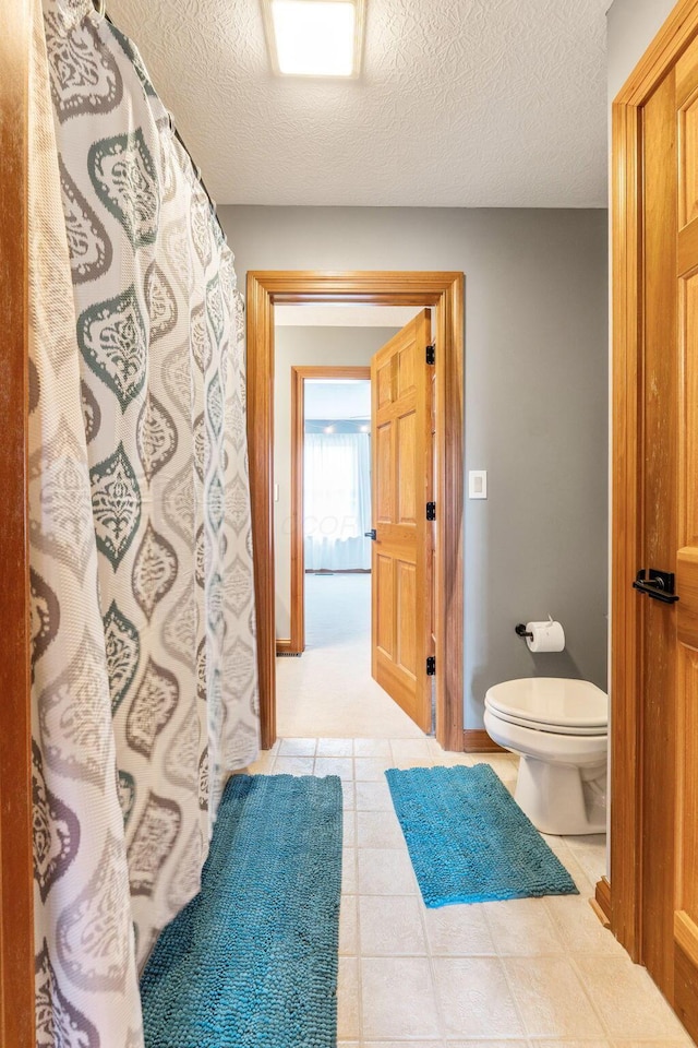 full bath with a textured ceiling, toilet, a shower with shower curtain, tile patterned floors, and baseboards
