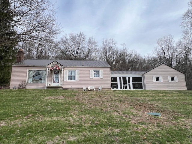 view of front of property with metal roof, a chimney, a sunroom, and a front lawn