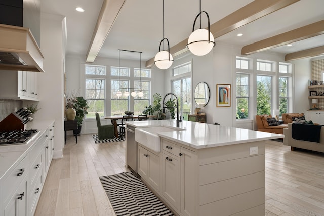 kitchen featuring a sink, open floor plan, light wood-style floors, beam ceiling, and custom range hood