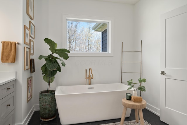 full bathroom with a freestanding tub, vanity, and baseboards