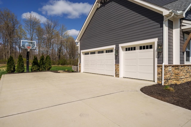 view of side of property featuring a shingled roof, concrete driveway, a garage, and stone siding