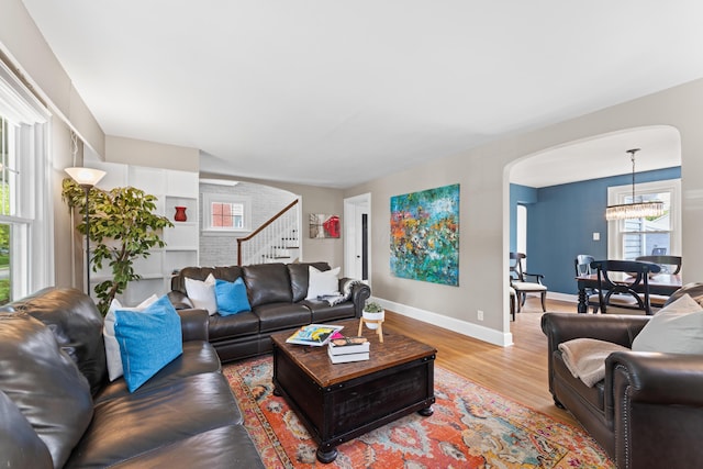 living area featuring arched walkways, stairway, light wood-style floors, a chandelier, and baseboards