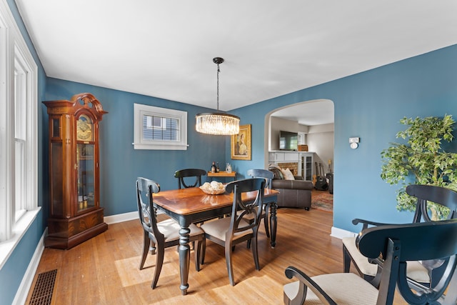 dining room featuring arched walkways, light wood-style flooring, baseboards, a chandelier, and plenty of natural light